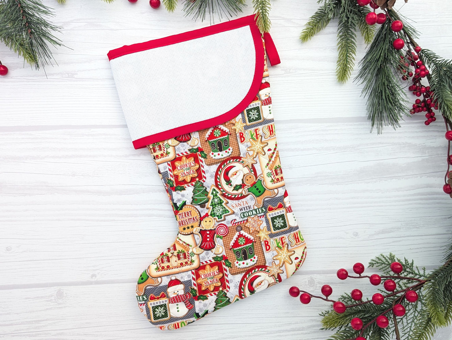 Christmas stocking with gingerbread design on a white wooden background with greenery and berries.