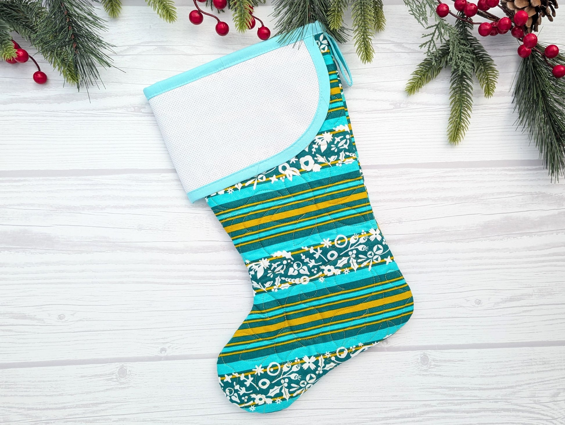 Colorful striped and patterned Christmas stocking on a white wooden surface with holiday decorations.
