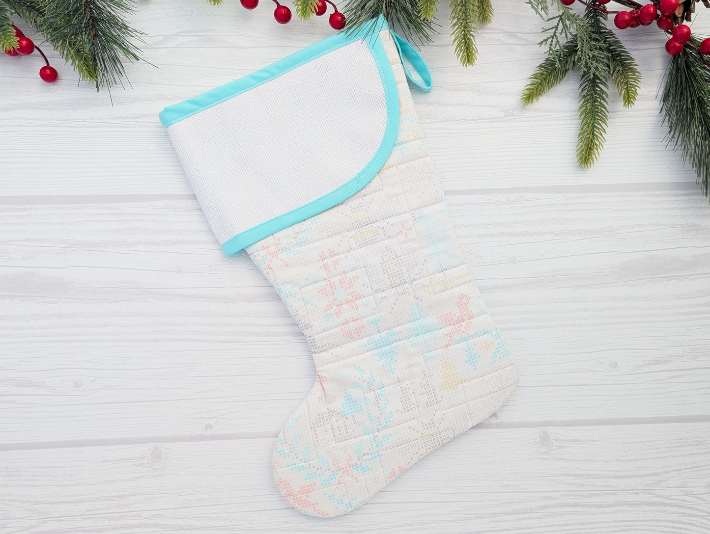 Quilted Christmas stocking with pastel patterns on a white wooden surface with holiday decorations.