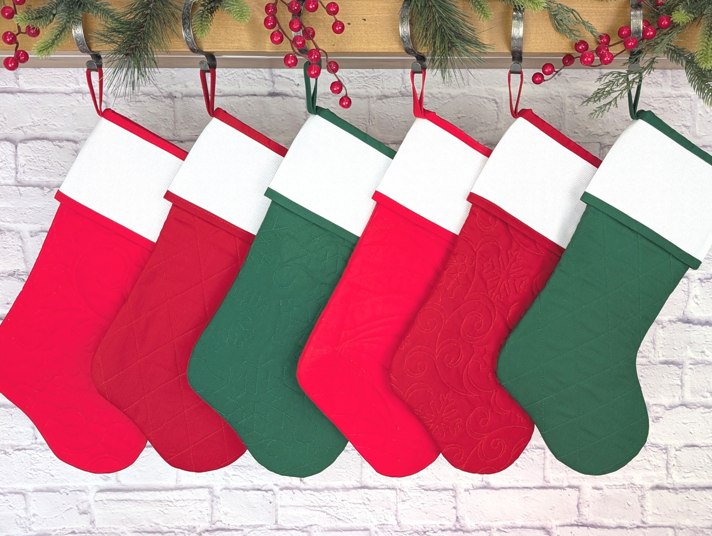 Set of red and green Christmas stockings hanging against a white brick wall.