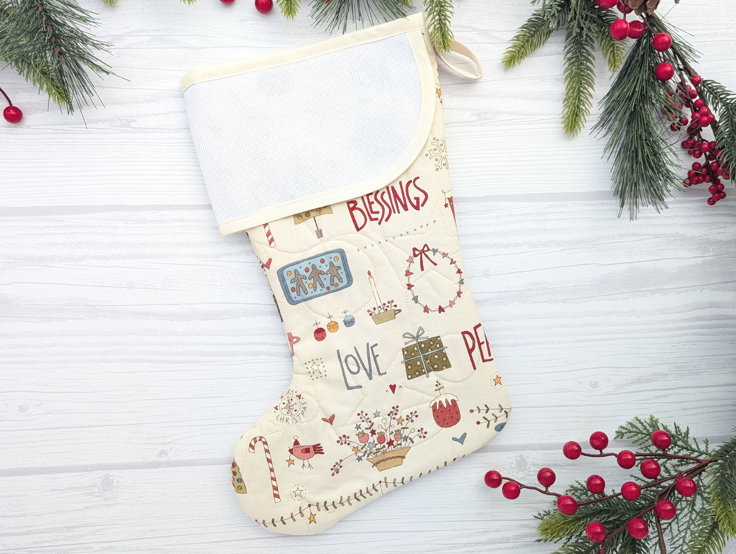 Decorative Christmas stocking with text and patterns on a white wooden background with holly.